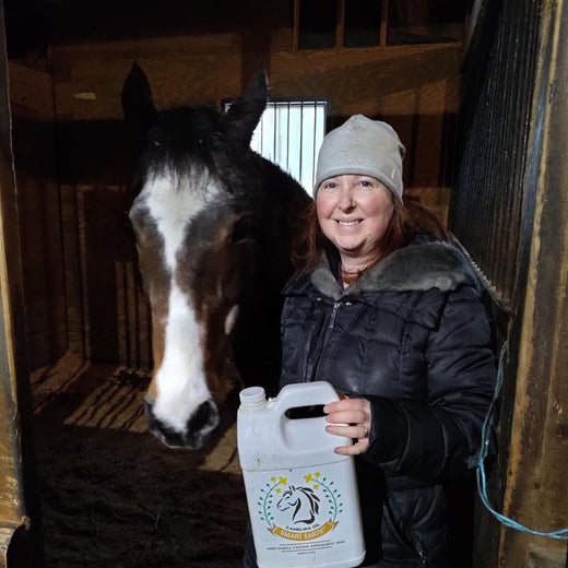Amy B. in the barn with Robin, her Quarter Horse, holding a 1-gallon jug of Camelina Oil