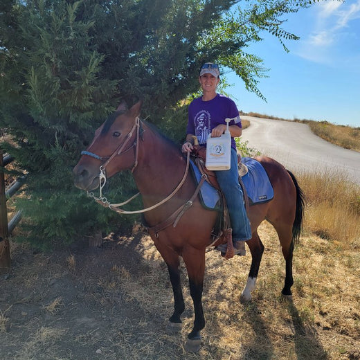Ginger S. mounted on her bay horse on the trail, holding a jug